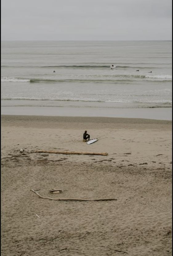 Surfer sitting on the beach with a surfboard near the waves at Westport, Washington
